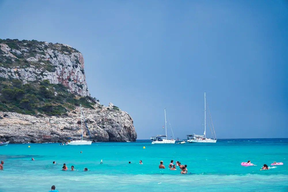 Playa de Son Bou en Menorca con aguas turquesas y bañistas disfrutando del mar
