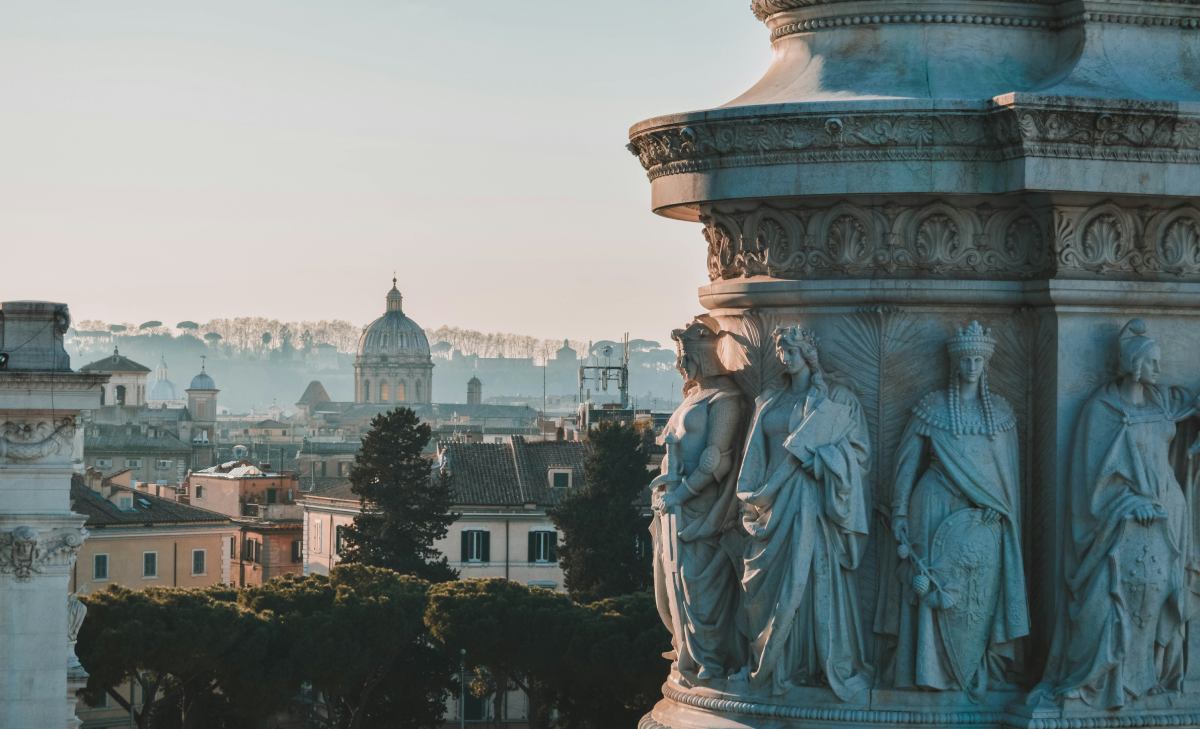 Vista panorámica de Roma al amanecer, con esculturas de mármol en primer plano y la cúpula de San Pedro al fondo.