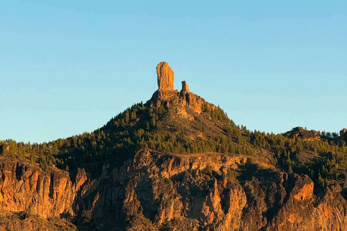 Vista del Roque Nublo en Gran Canaria iluminado por el sol del atardecer, rodeado de pinares y formaciones volcánicas.