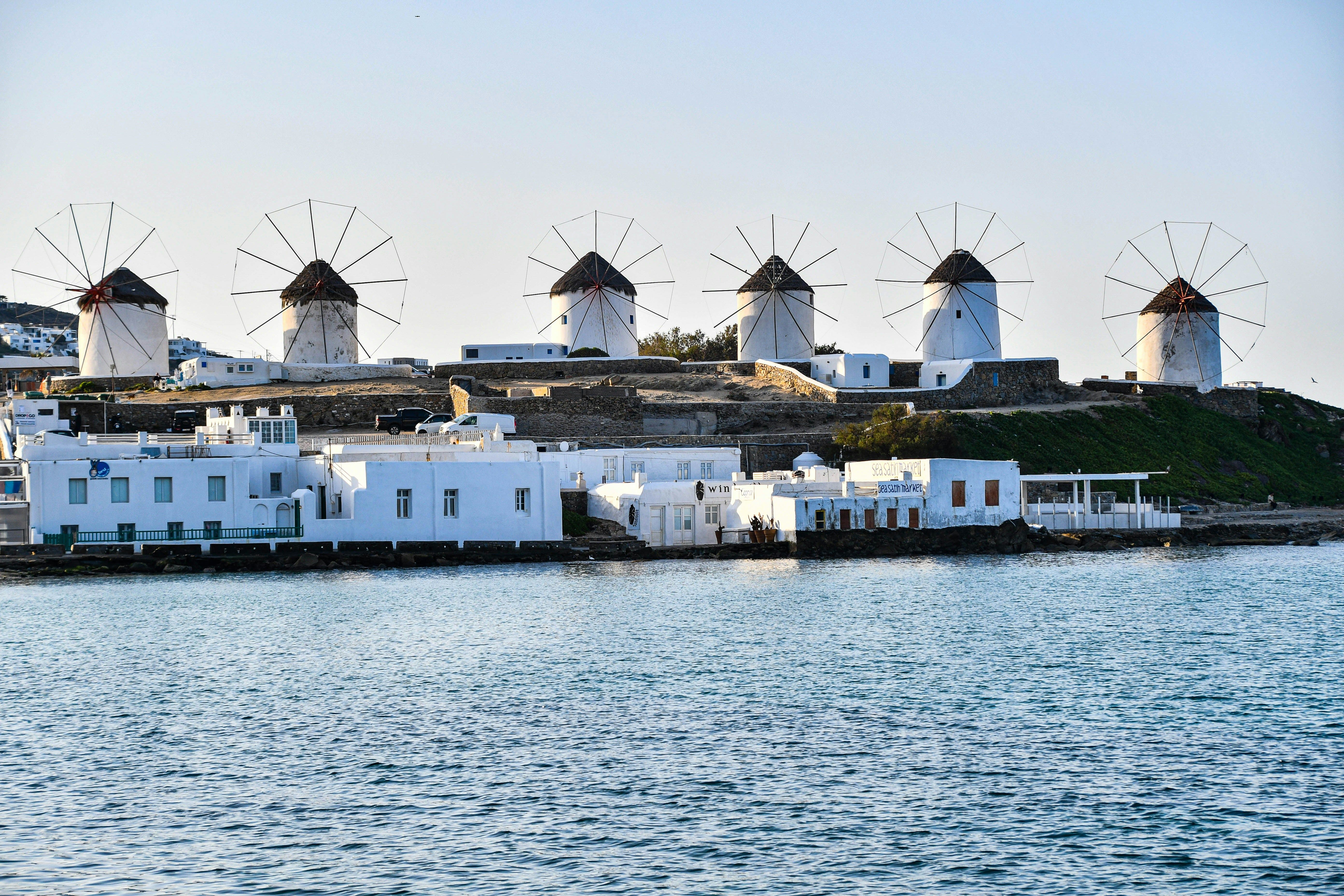 windmills lined up on a hill with the sea below