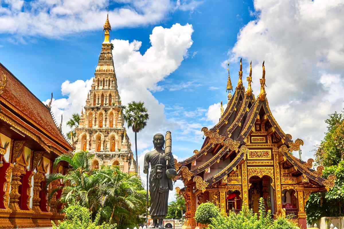 Templos budistas decorados con detalles dorados y una estatua de Buda en Chiang Mai, Tailandia, bajo un cielo azul con nubes.