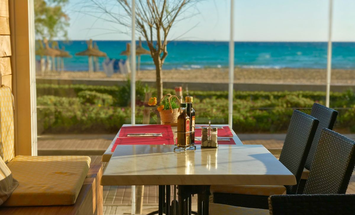 Mesa preparada en la terraza de un restaurante frente al mar en las Islas Baleares, con vistas a la playa y el Mediterráneo al fondo