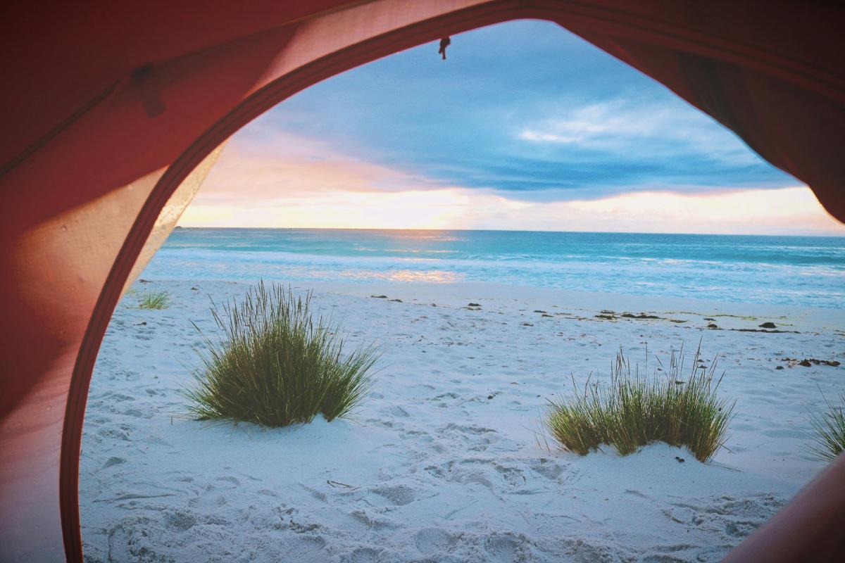 Vista de la playa al amanecer desde una tienda de campaña en Mallorca, experiencia de camping sostenible junto al mar