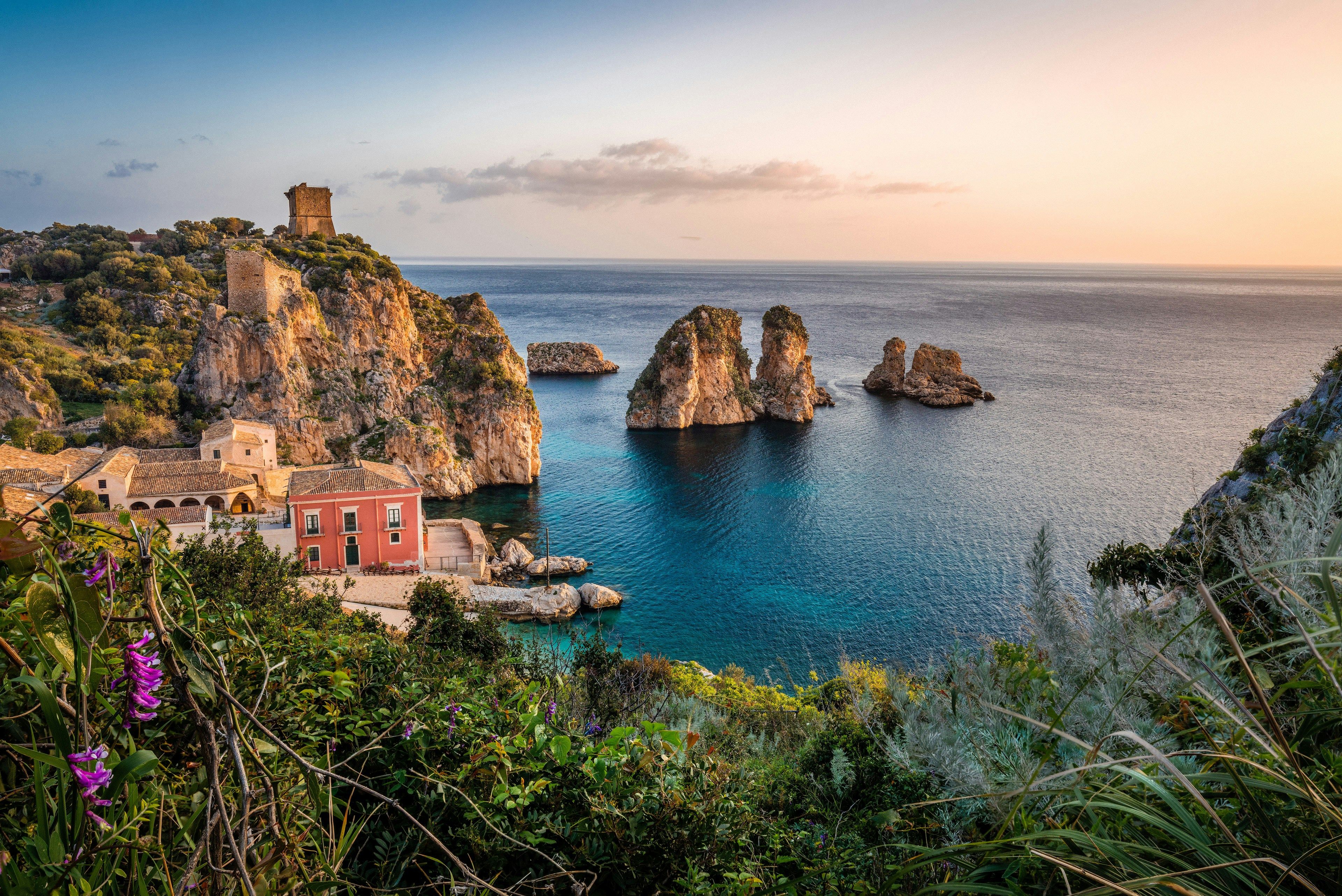 Antiguo pueblo pesquero de Tonnara di Scopello en Sicilia, Italia, rodeado de formaciones rocosas en el mar y un paisaje costero al atardecer.