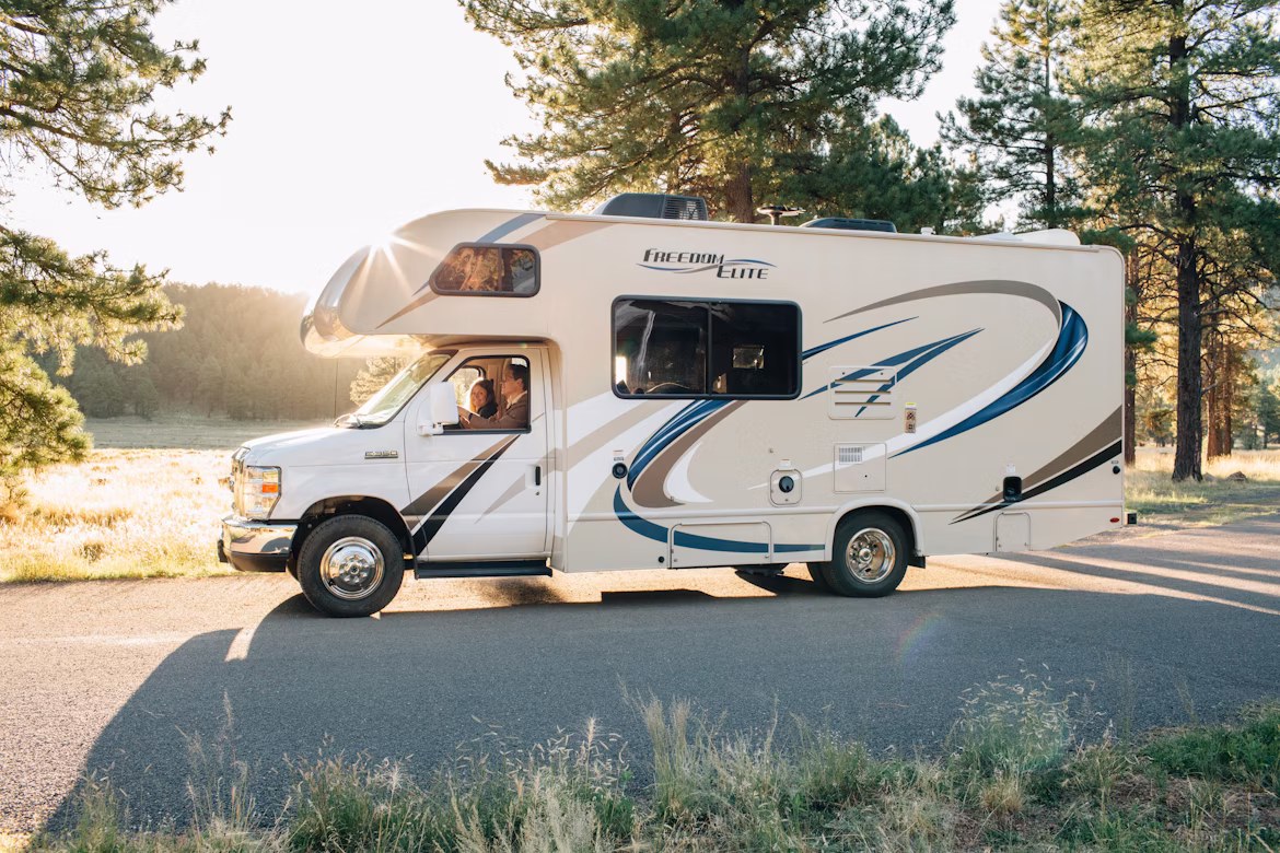two people in a caravan driving along a road next to some trees