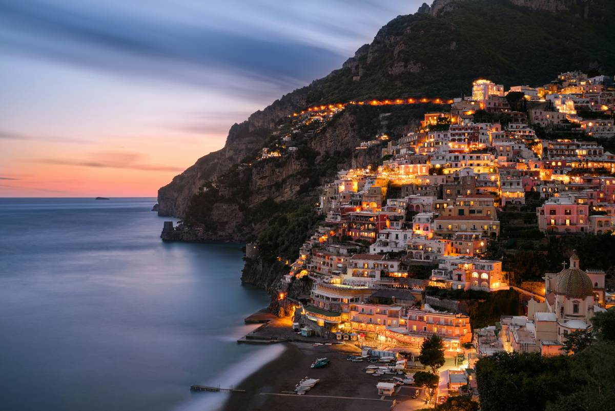 Positano iluminado al anochecer con el perfil de la Costa Amalfitana recortado sobre el mar Tirreno