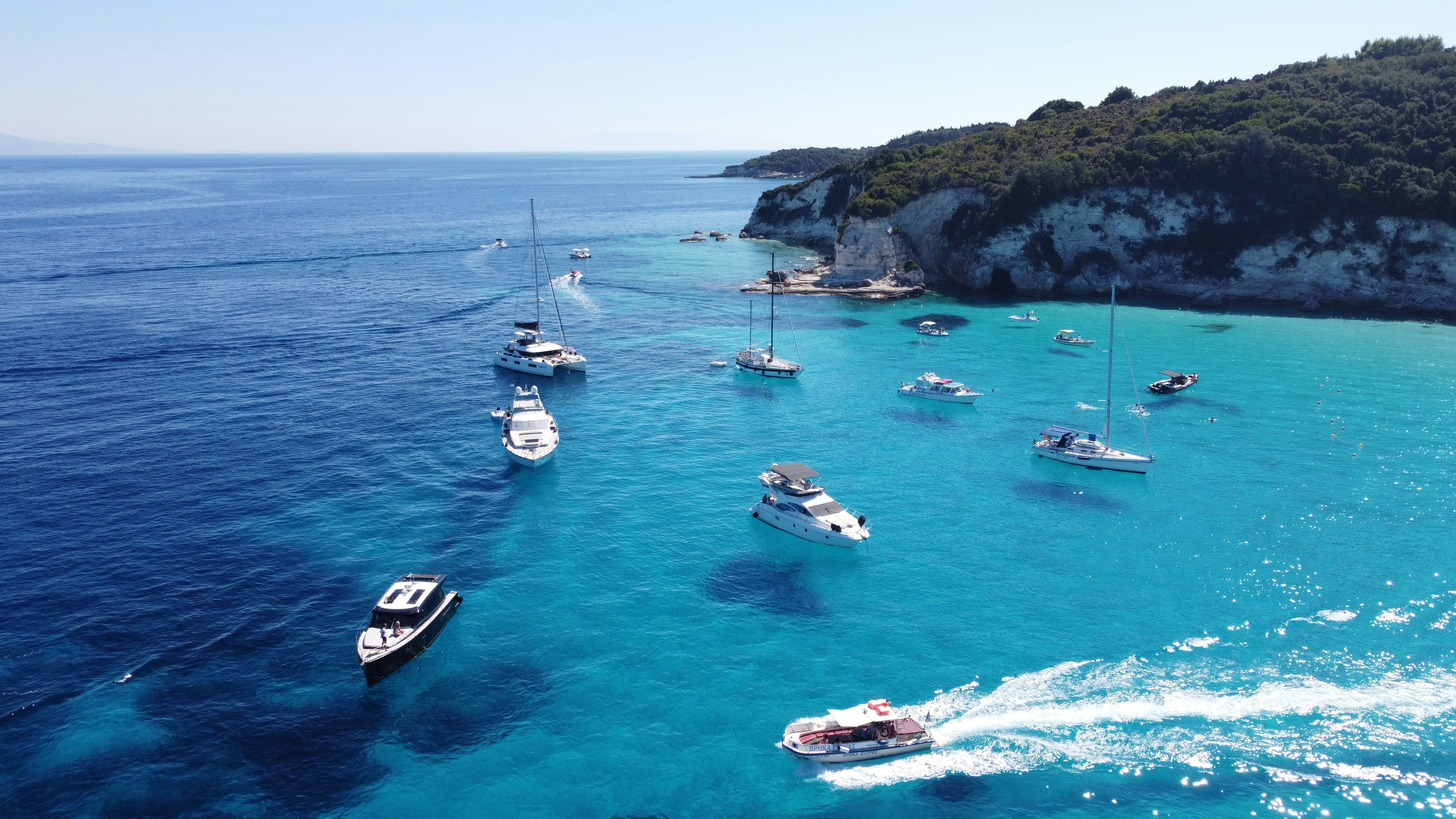 mer claire avec bateaux blancs et falaises au fond